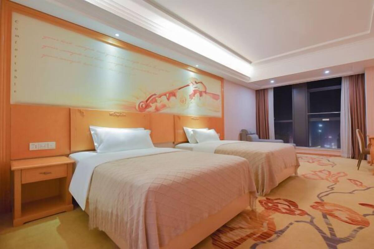 A hotel room with two beds, a large wall mural, and a view of the city at night.