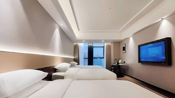 Ein Hotelzimmer mit zwei Betten, einem an der Wand montierten Fernseher und einem Fenster mit Blick auf die Stadt.