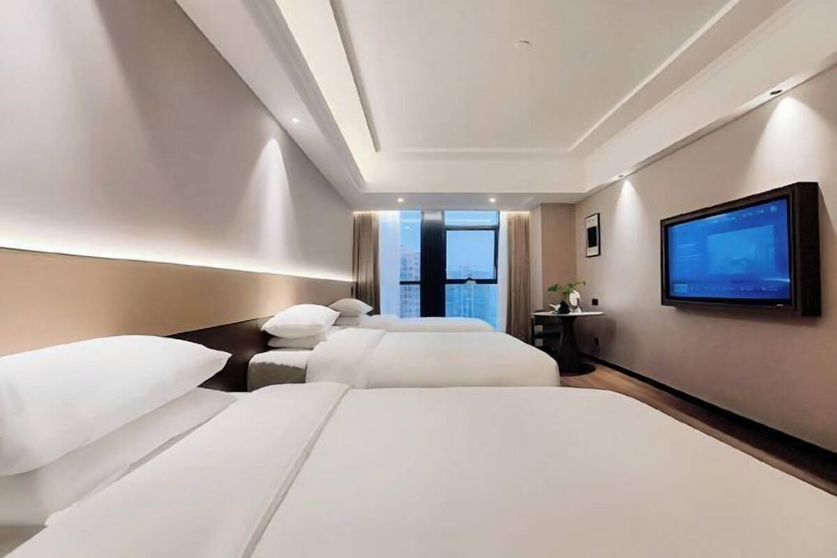 A hotel room with two beds, a television mounted on the wall, and a window providing a view of the cityscape.