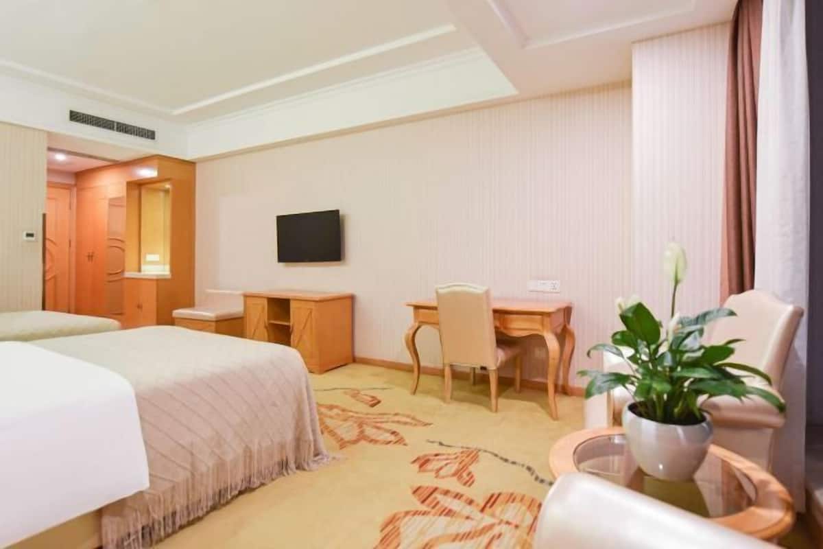 A hotel room with a bed, a desk, a chair, a television, and a potted plant.