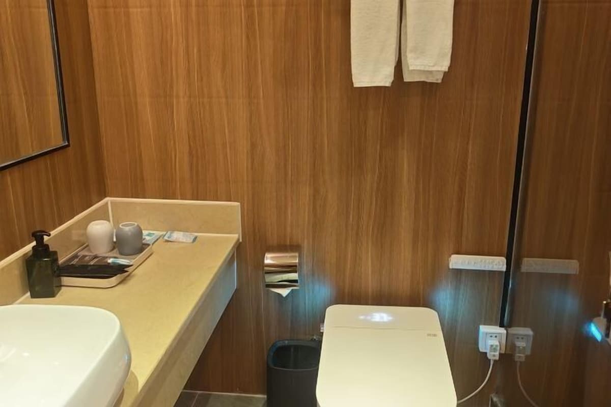 A bathroom with a wooden vanity, a sink, a toilet, and a trash bin.