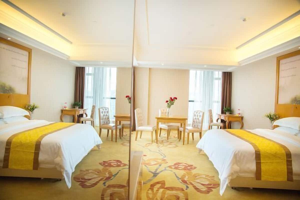 A hotel room with two beds, a small table with chairs, and a large mirror.