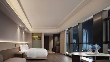 A modern hotel room with a large bed, a seating area, and a view of the cityscape through large windows.