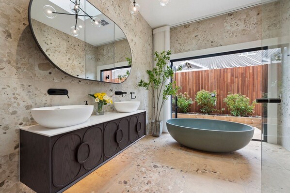 Un baño moderno con un espejo redondo grande, dos lavamanos y una bañera espaciosa.