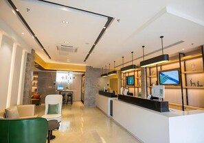 A modern hotel lobby with a reception desk, seating area, and a view into the dining area.