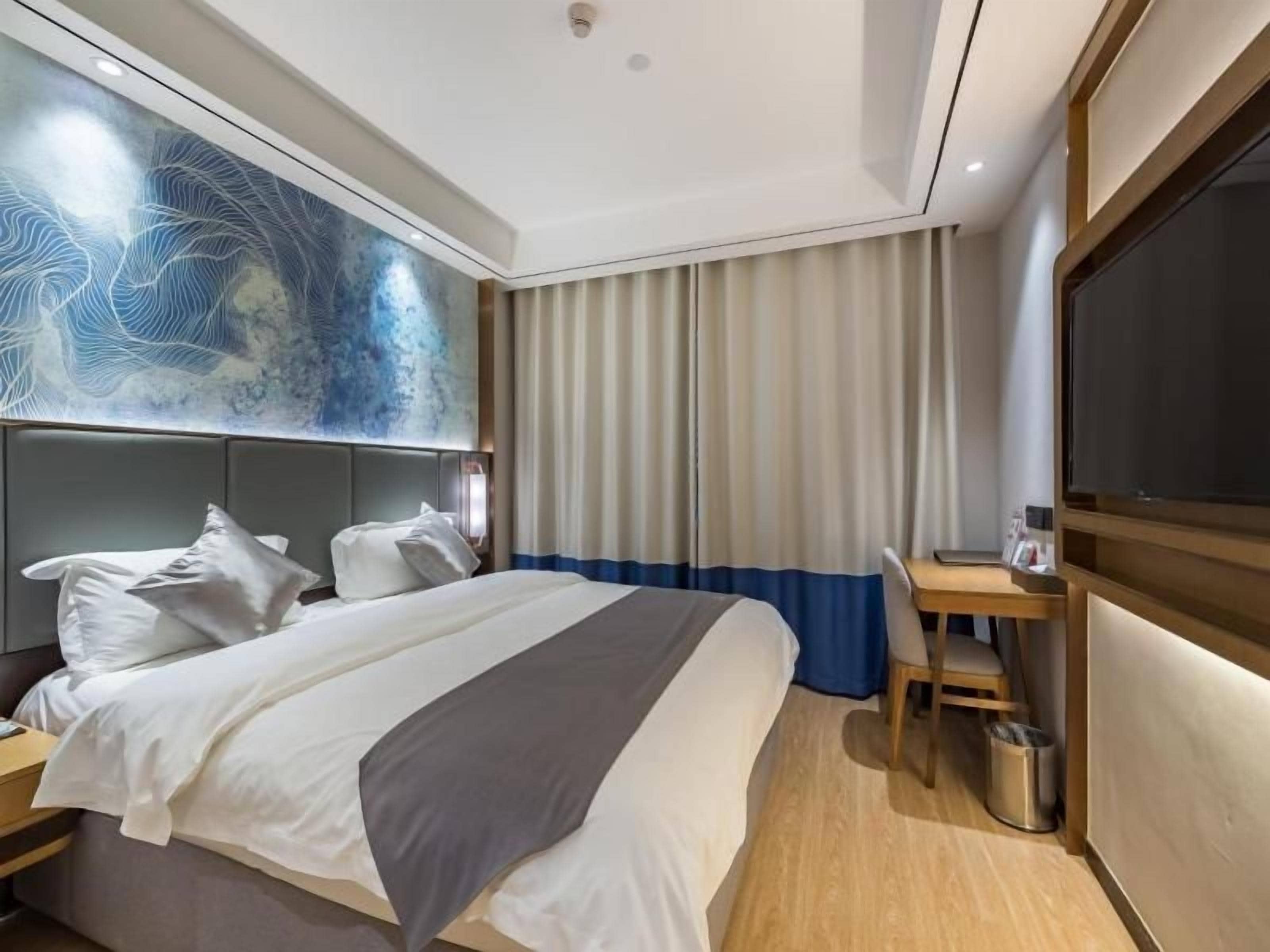 A hotel room with a bed, a desk, a chair, a TV, and a wall with a decorative design.