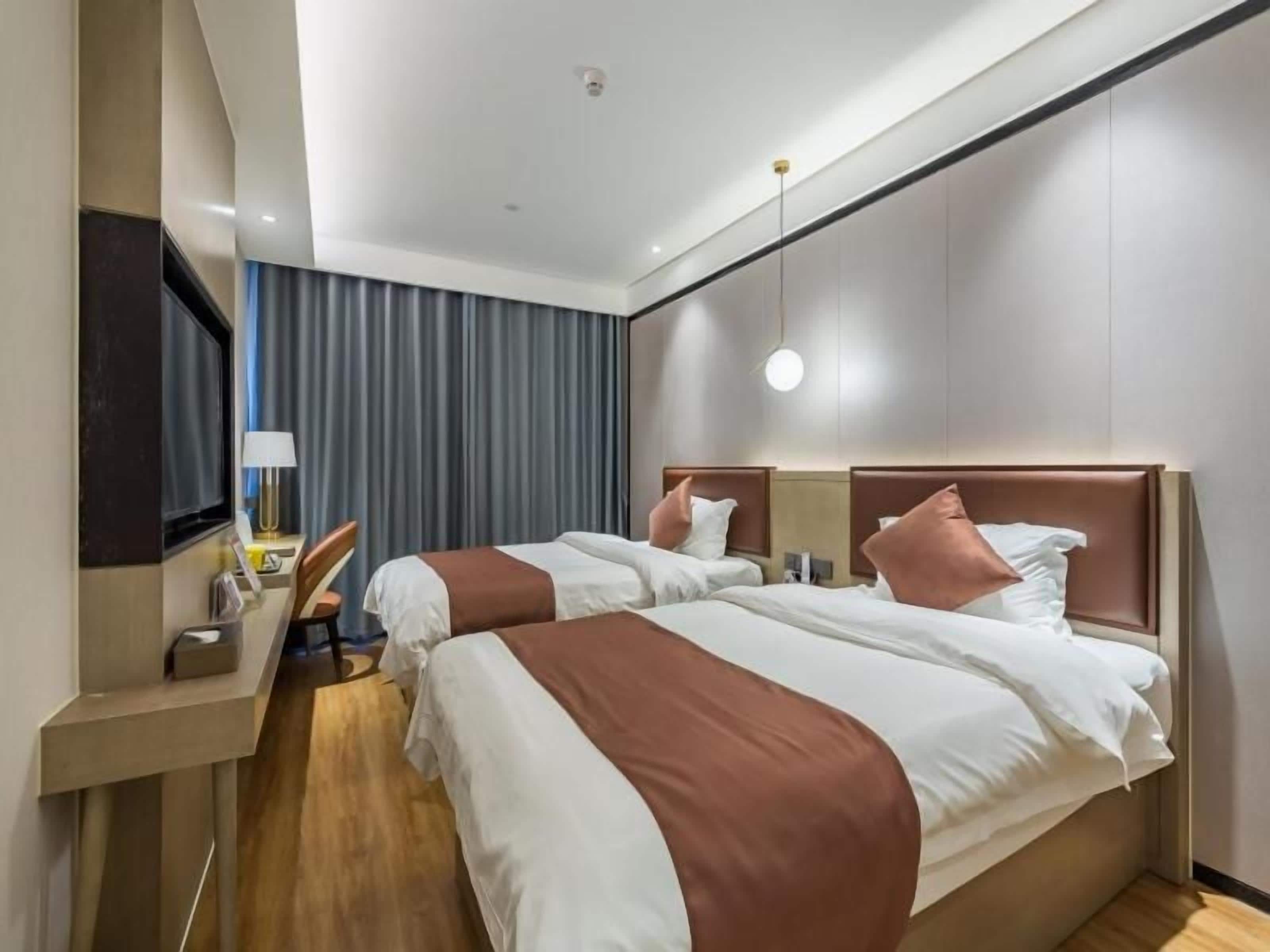 A hotel room with two beds, a desk, a chair, and a TV.