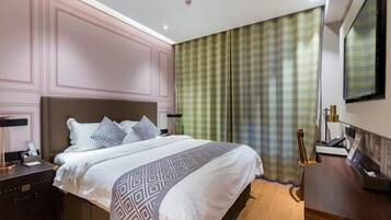A hotel room with a large bed, bedside tables, a desk, and a television.