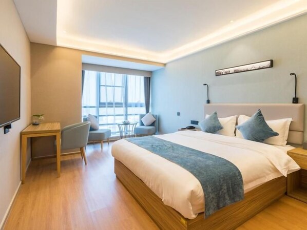 A modern hotel room with a large bed, a desk, and a seating area by the window.