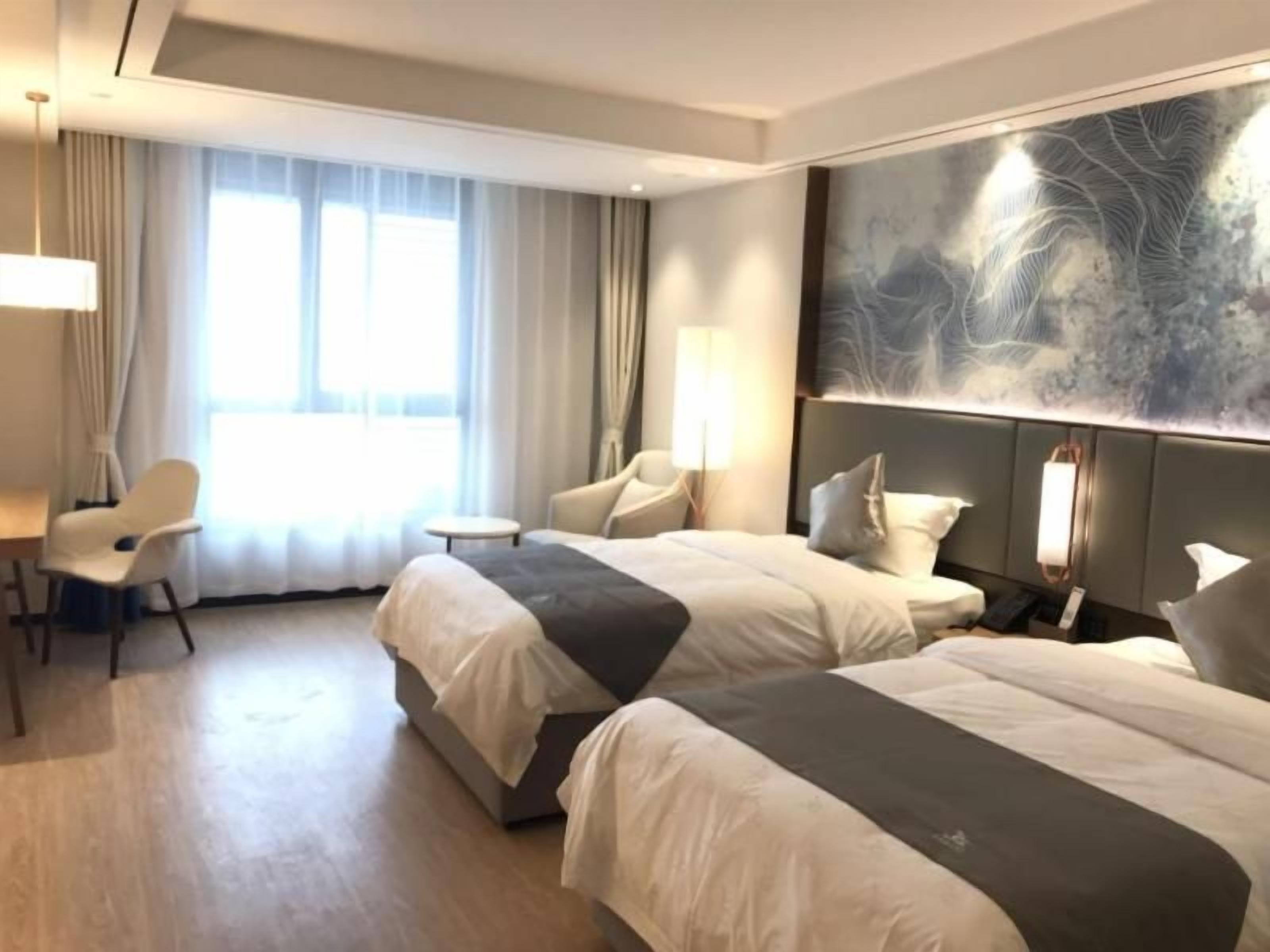 A hotel room with two beds, a desk, a chair, and a large abstract painting on the wall.
