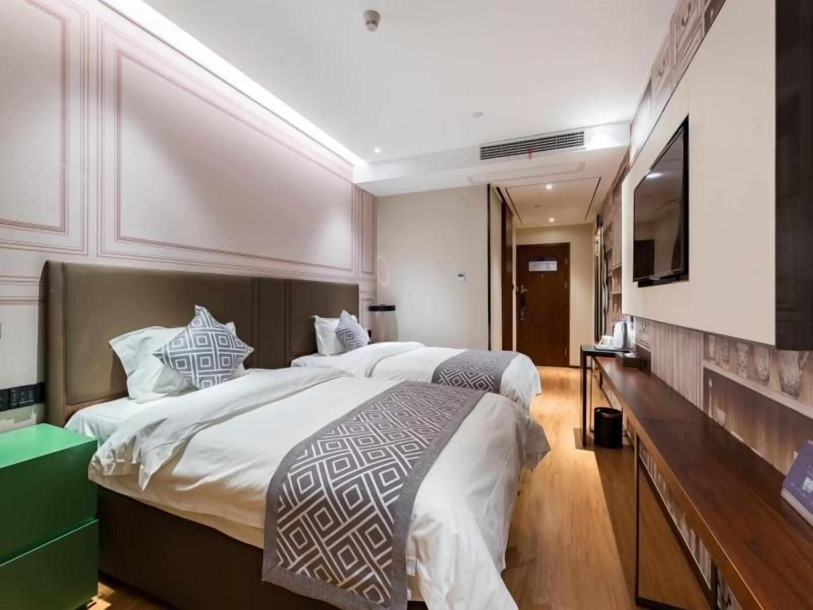 A hotel room with a large bed, bedside tables, a dresser, and a mirror.