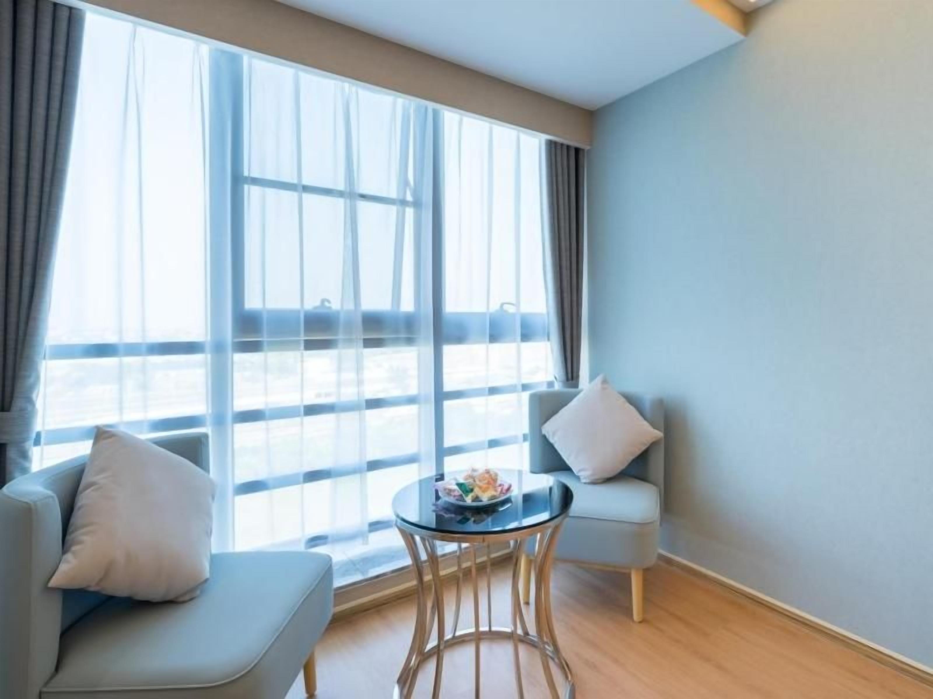 Una habitación con dos sofás, una mesita redonda y un amplio ventanal con cortinas.