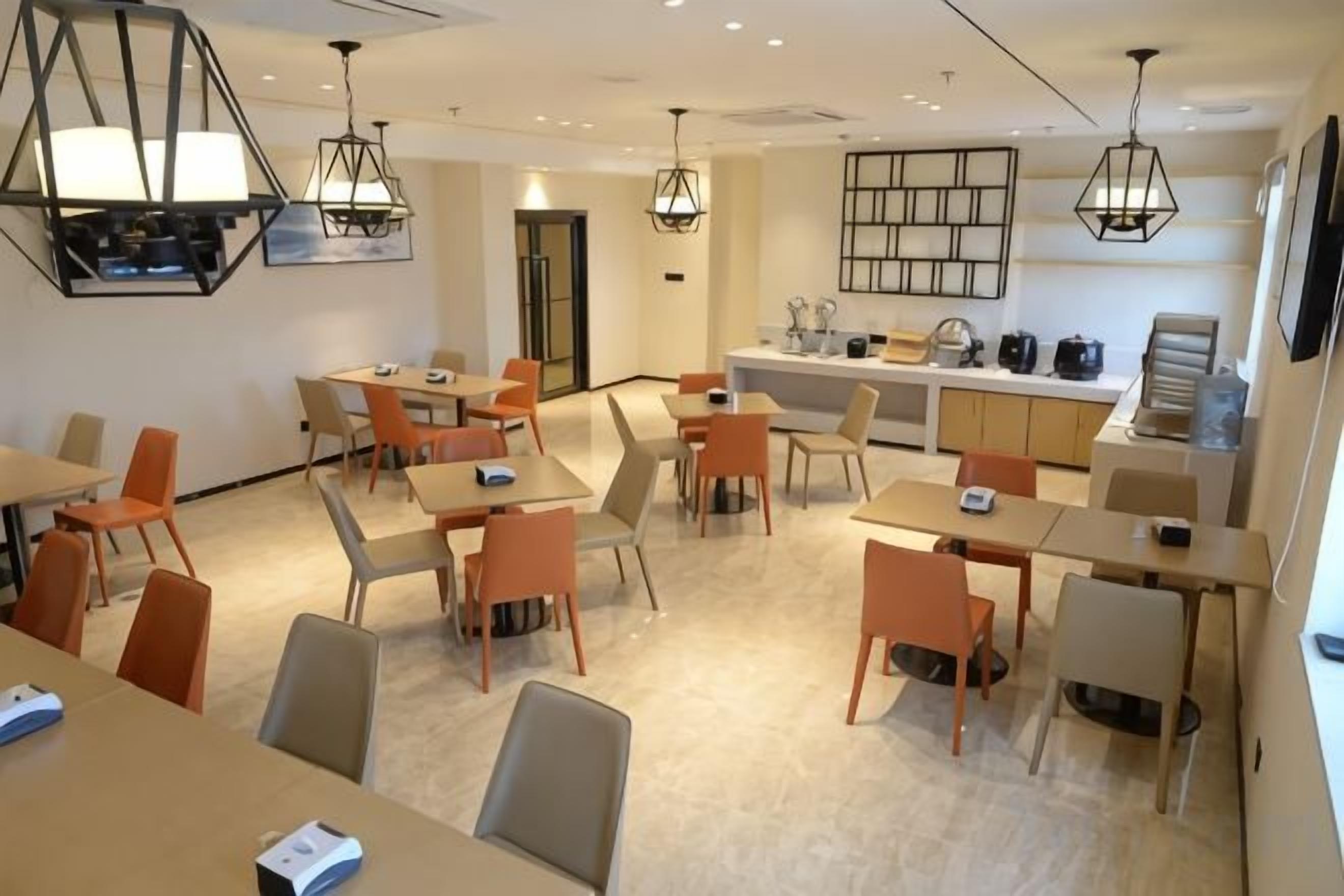 Un comedor de hotel con varias mesas y sillas, una zona de cocina e iluminación colgante.