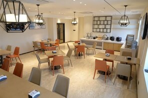 A hotel dining area with multiple tables and chairs, a kitchen area, and pendant lighting. - City Comfort Inn (Zhongshan Dongfeng Town Government) (Zhongshan)