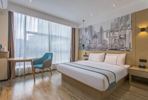 A hotel room with a bed, a chair, a table, a cityscape mural, and a large window.