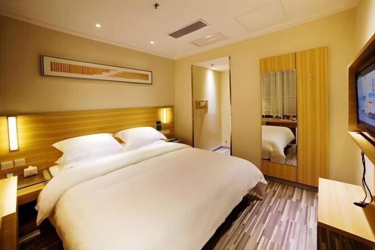 Ein Hotelzimmer mit einem großen Bett, Nachttischen, einem Spiegel und einem Fernseher.