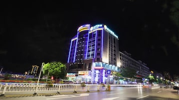 A multi-story hotel with illuminated signage, a pedestrian crossing, and a busy street at night.