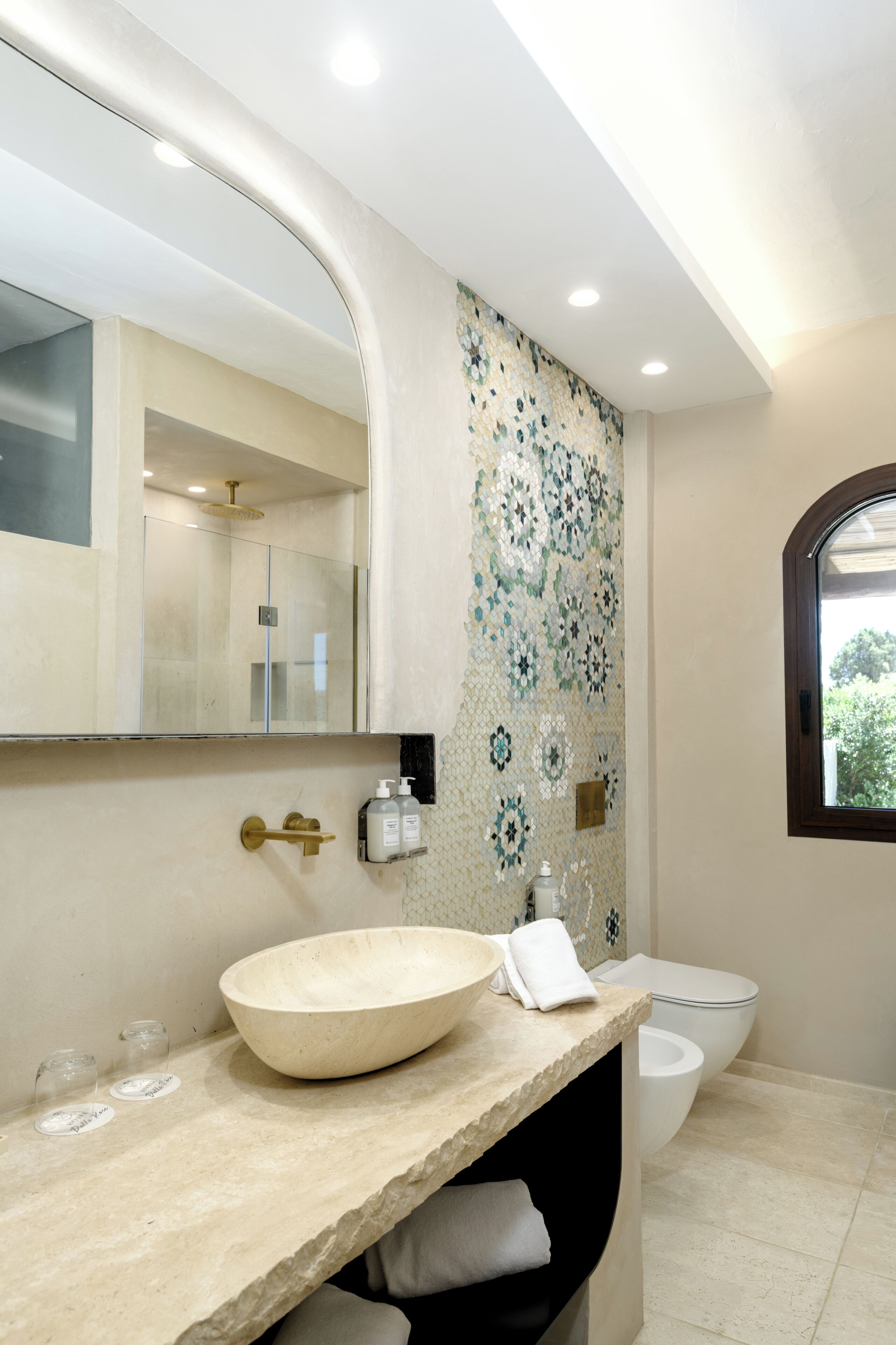 A bathroom with a large mirror, a vessel sink, a toilet, and a window.
