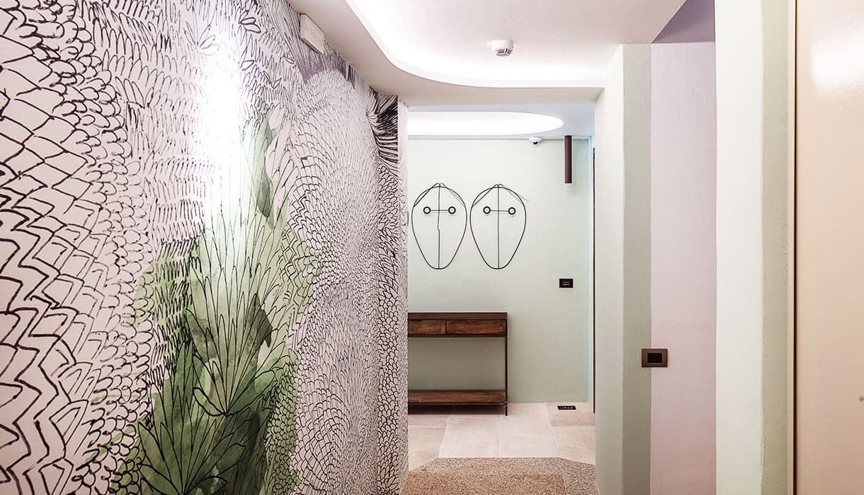 Un pasillo con un papel tapiz decorativo, un banco de madera y un baño minimalista con dos espejos ovalados.