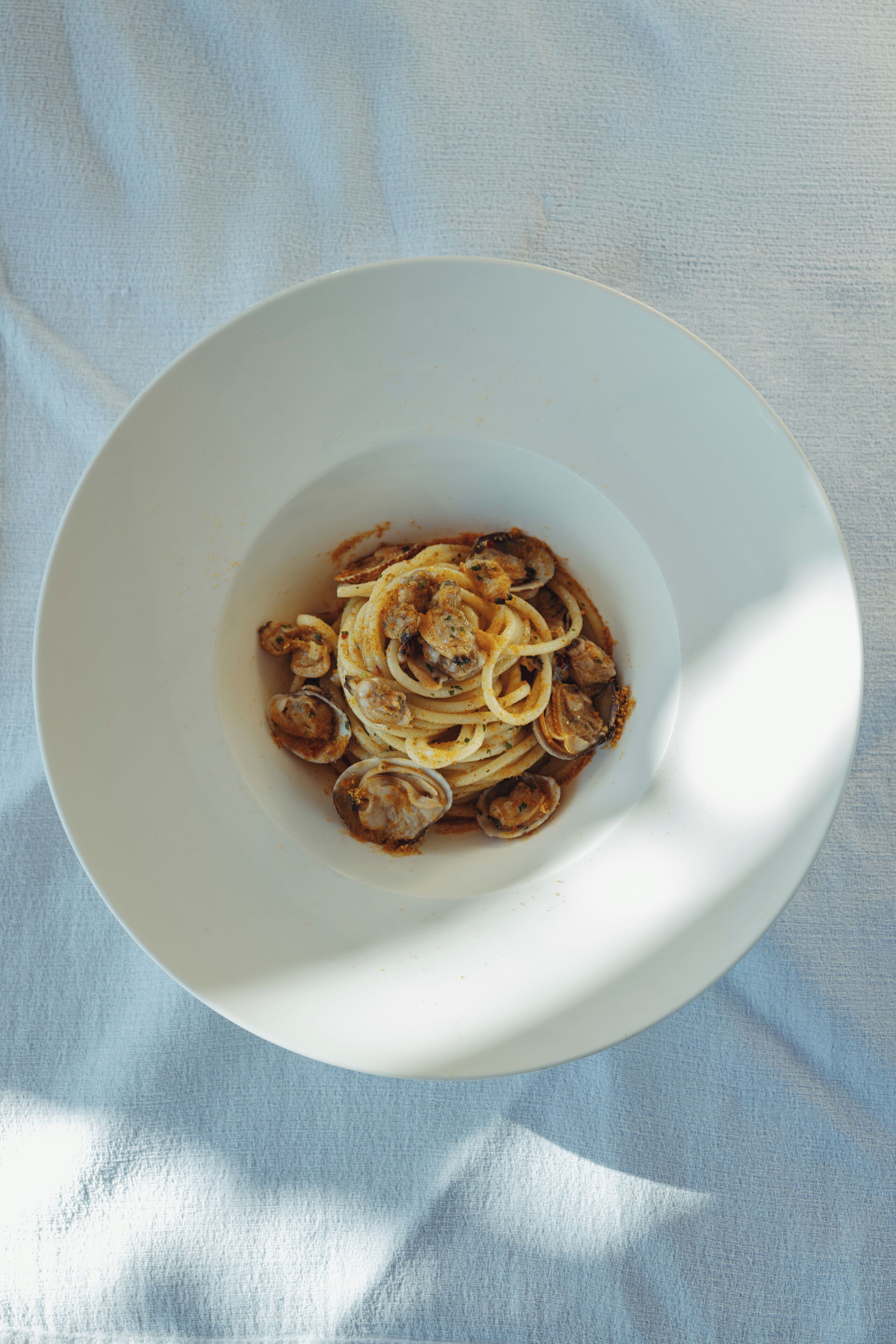 A white bowl containing a pasta dish with a sauce, placed on a textured surface.