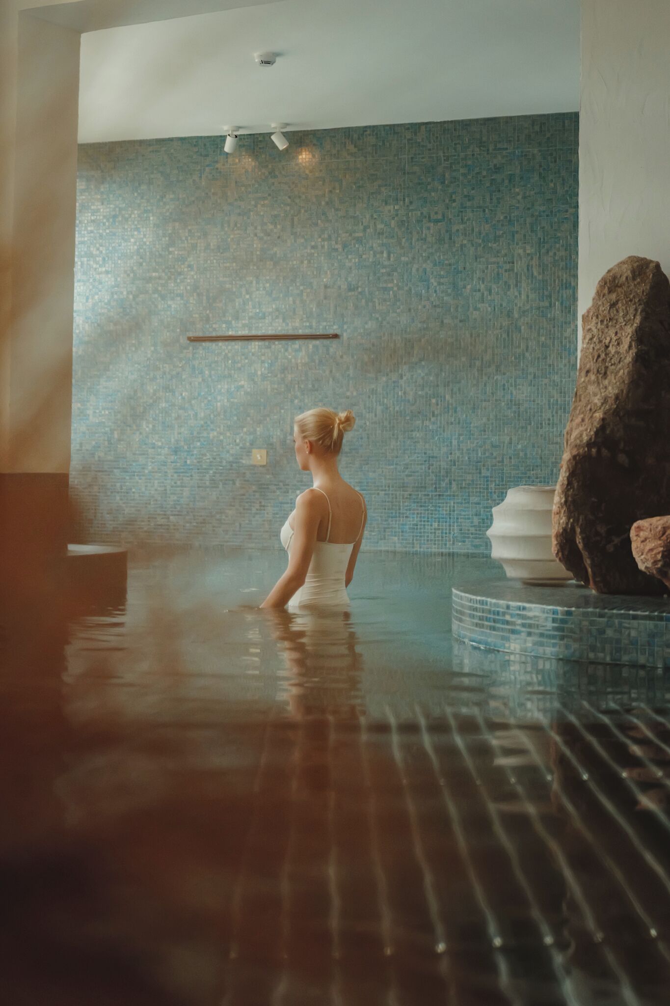 A woman in a swimming pool with a tiled wall and a large rock.