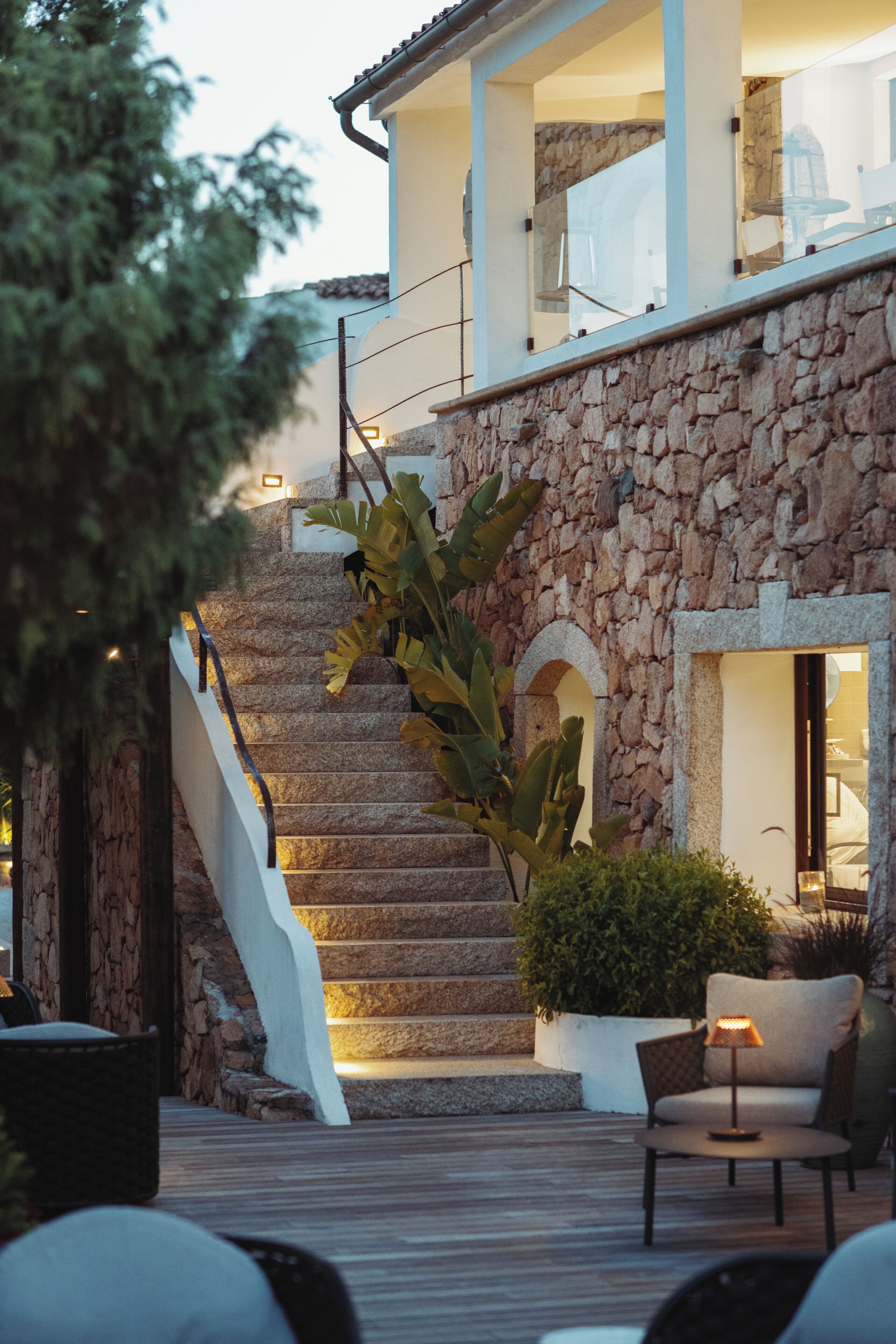A stone staircase leading to a second floor, a wooden deck with outdoor seating, and a large plant.