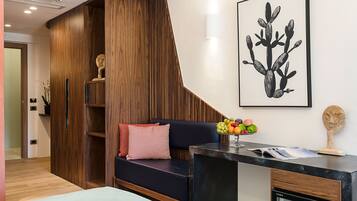 Una habitación de hotel moderna con una pared de acento de madera, un sofá negro con cojines, una mesita con un frutero y una obra de arte enmarcada en la pared.