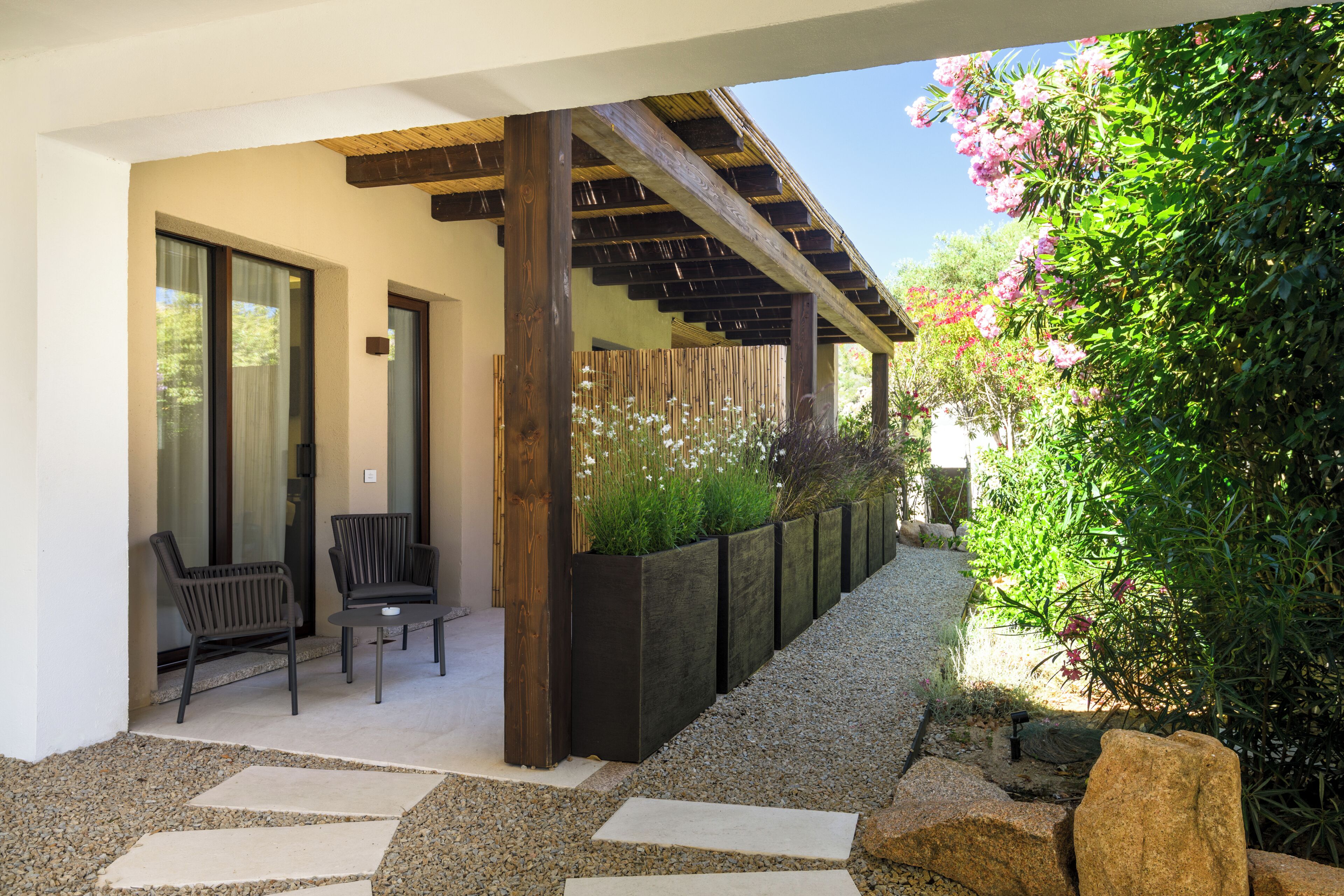 Un espacio al aire libre con sillas, una mesa, una pérgola y un jardín con plantas y flores.