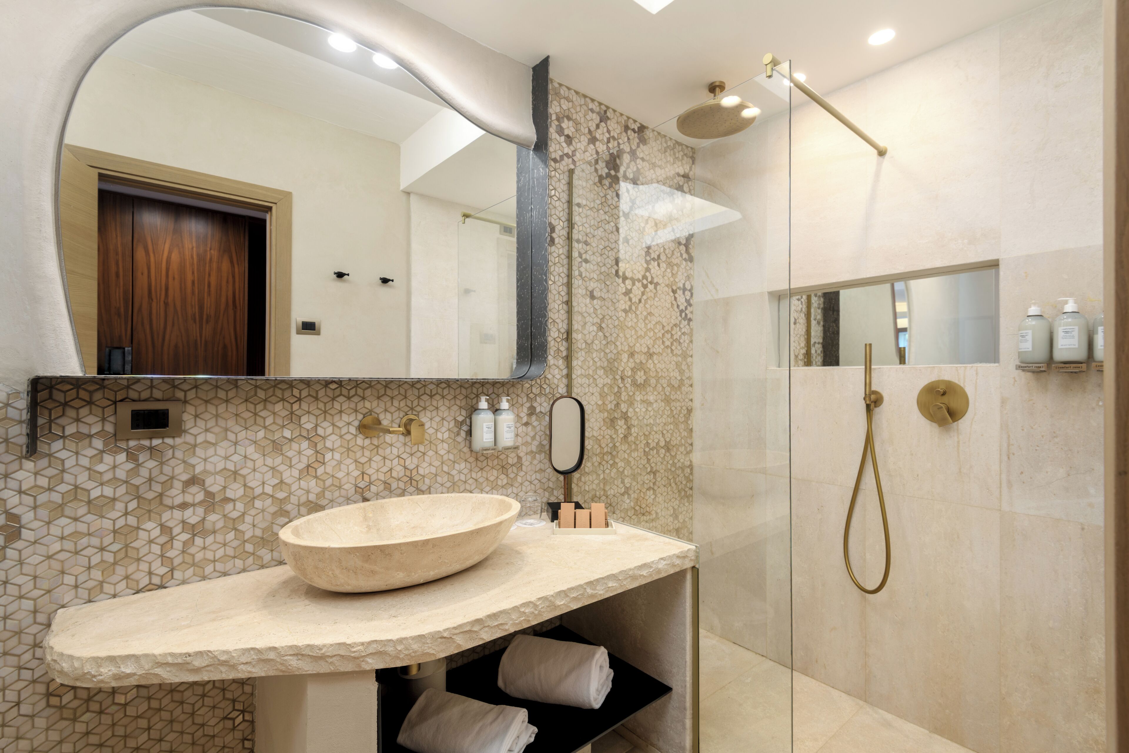 A modern bathroom with a stone sink, a glass shower enclosure, and a large mirror.