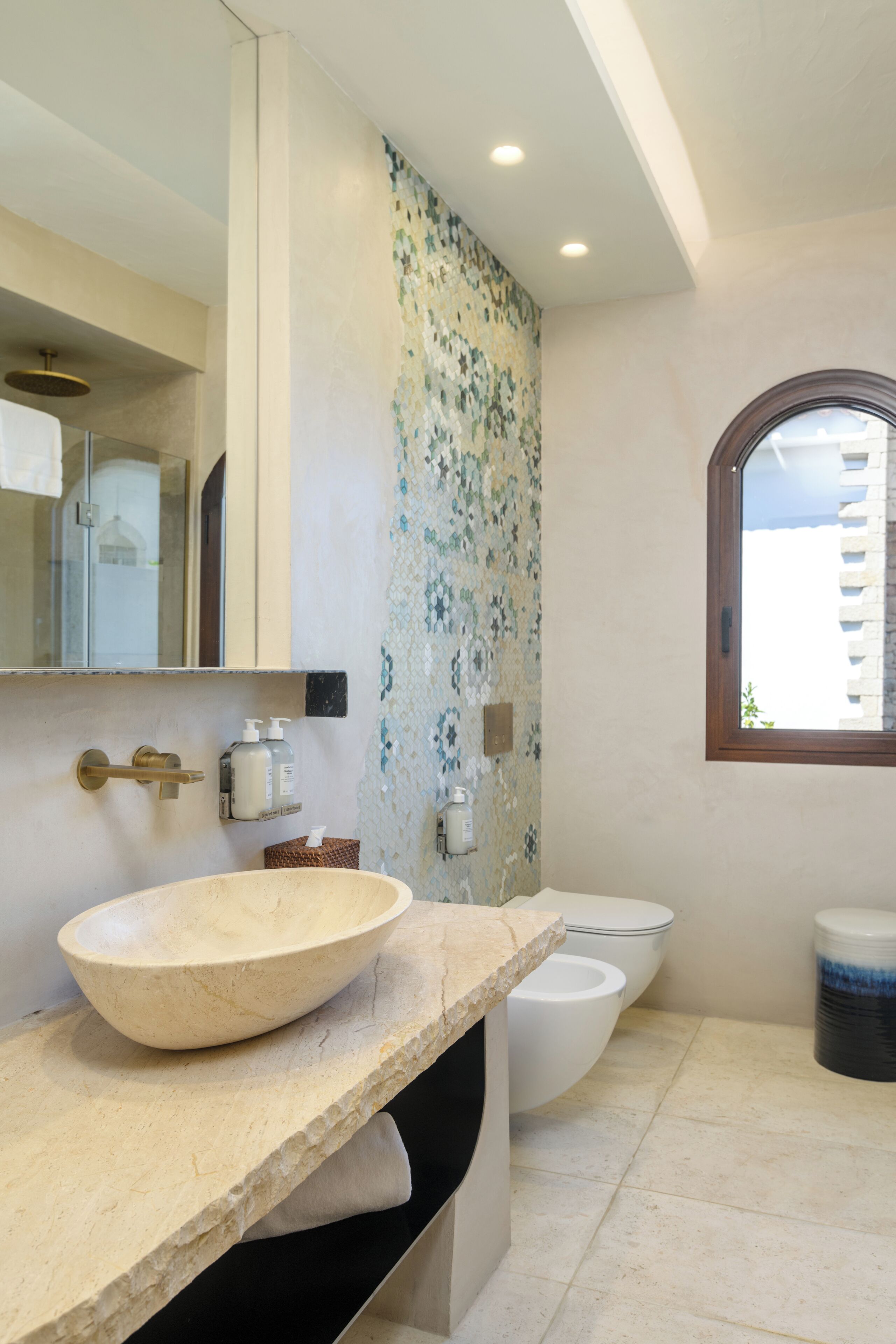 A bathroom with a large bowl sink, a toilet, a mirror, and a window.