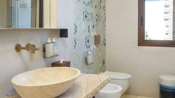 A bathroom with a large bowl sink, a toilet, a mirror, and a window.
