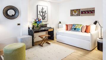A modern living room with a white sofa, a coffee table, and a desk with a chair. There are wall art pieces and a mirror on the wall.