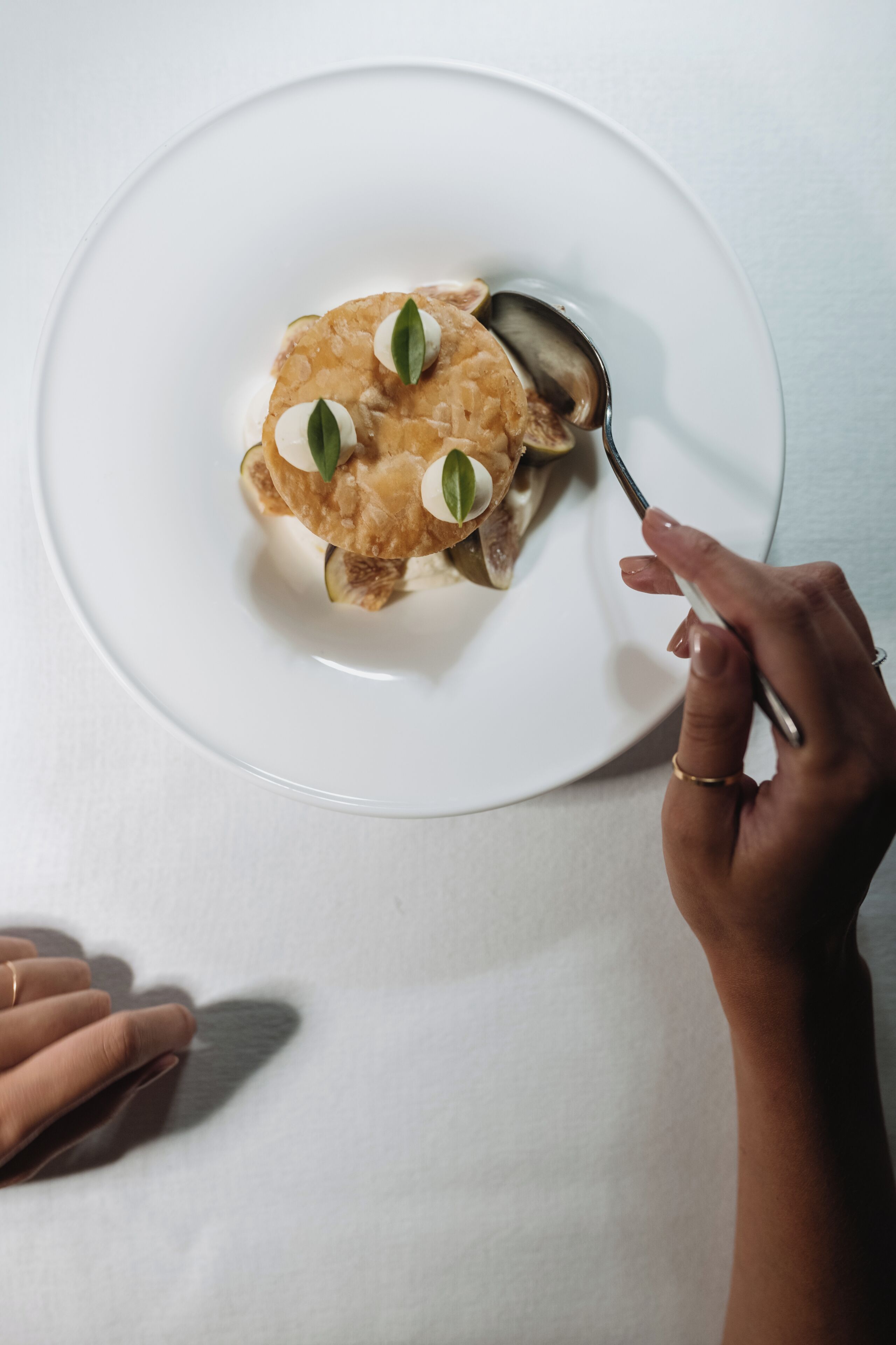 A white plate with a food item, a spoon, and a hand holding the spoon.