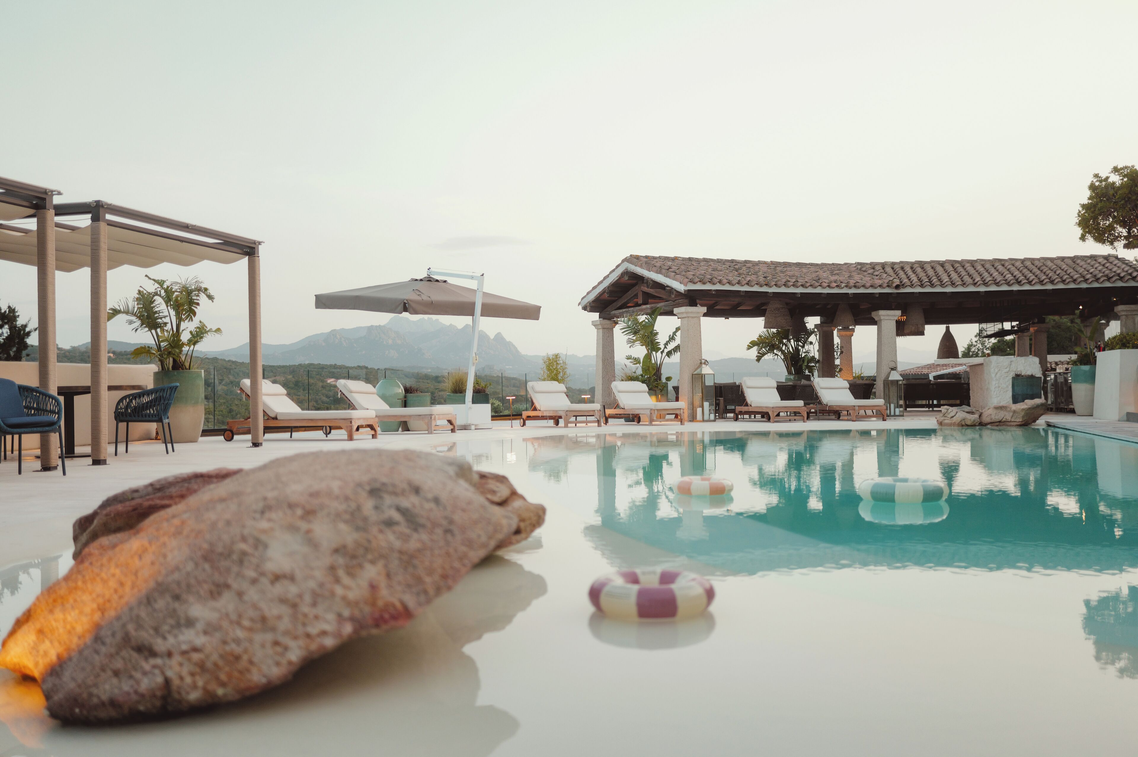 Un espace piscine avec des chaises longues, un coin salon abrité et une vue sur les montagnes en arrière-plan.