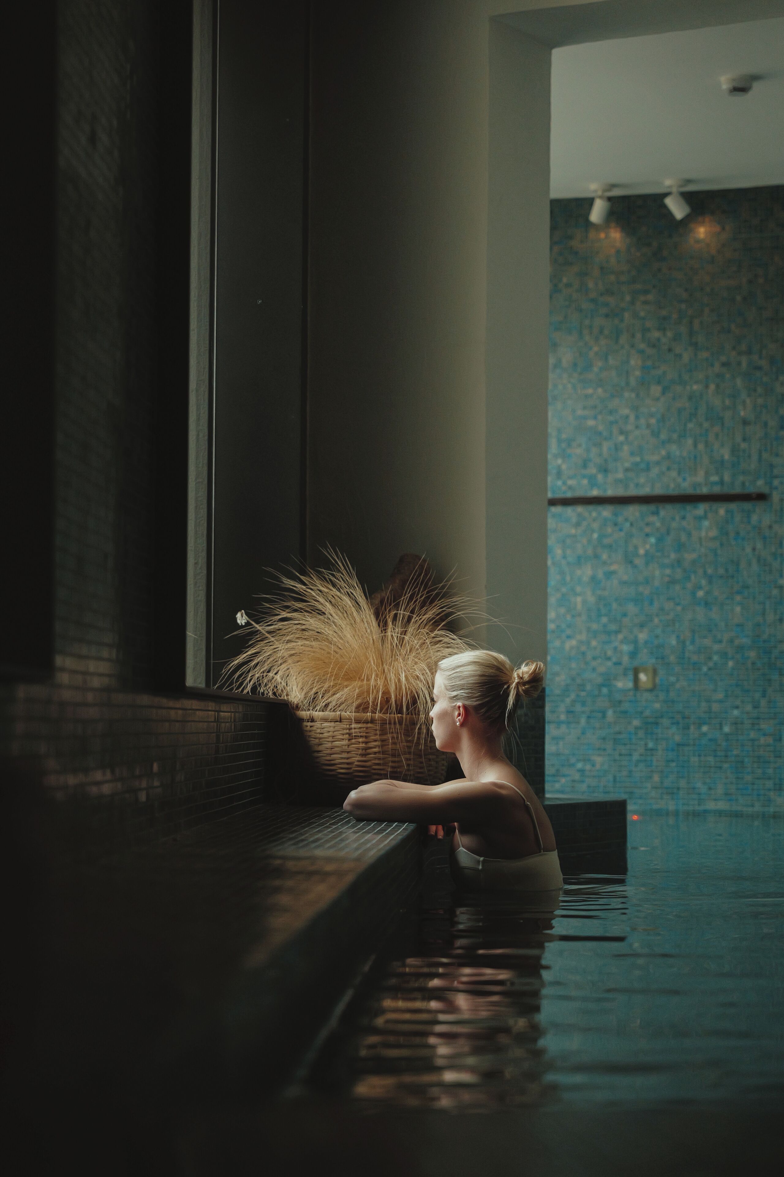 Una persona en una bañera con ventana y pared de azulejos azules al fondo.