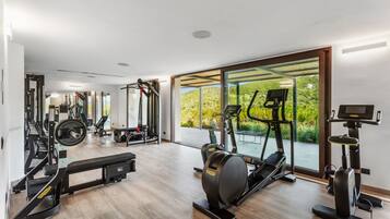 A modern gym with cardio machines, weightlifting equipment, and a large window offering a view of greenery.