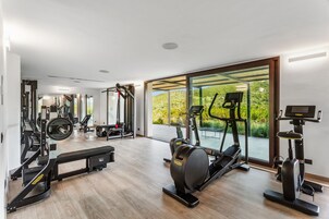 A modern gym with cardio machines, weightlifting equipment, and a large window offering a view of greenery.
