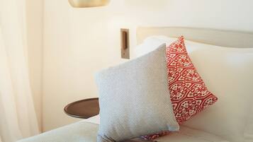 A bedroom with a bed, pillows, a hanging light fixture, and a wall hanging.