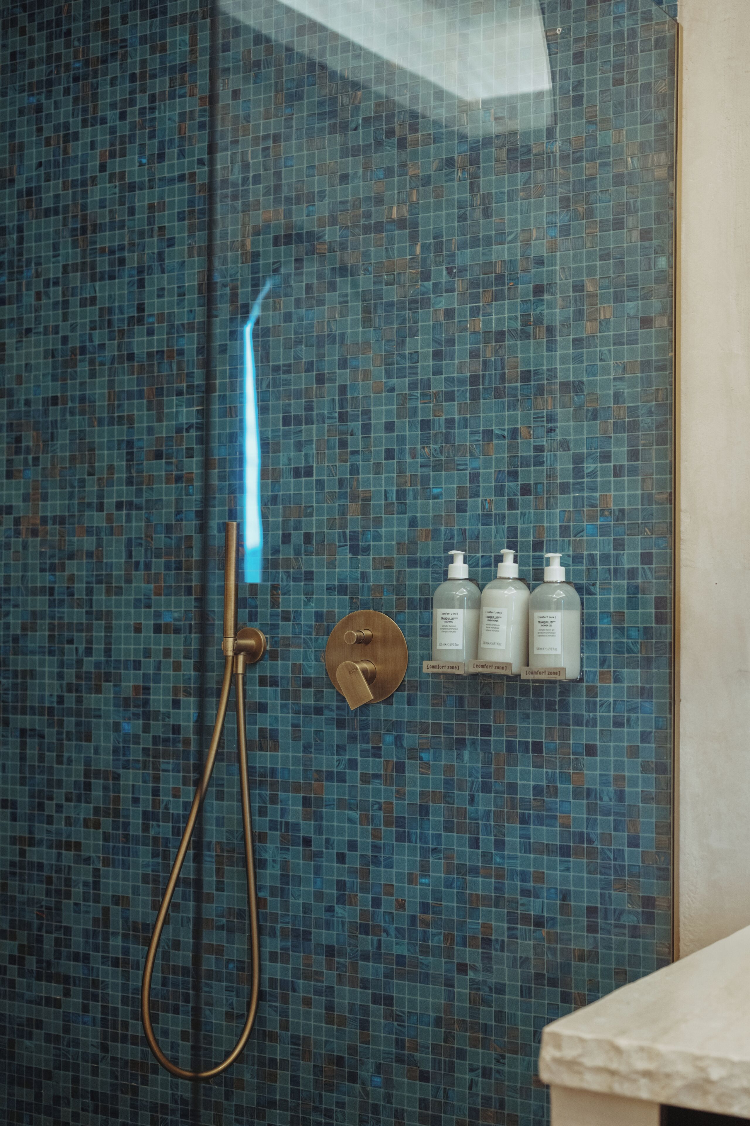 Ein Badezimmer mit Duschkabine, Handbrause und drei Flaschen mit der Aufschrift 'comfort zone' auf einem Regal.