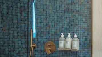 Ein Badezimmer mit Duschkabine, Handbrause und drei Flaschen mit der Aufschrift 'comfort zone' auf einem Regal.