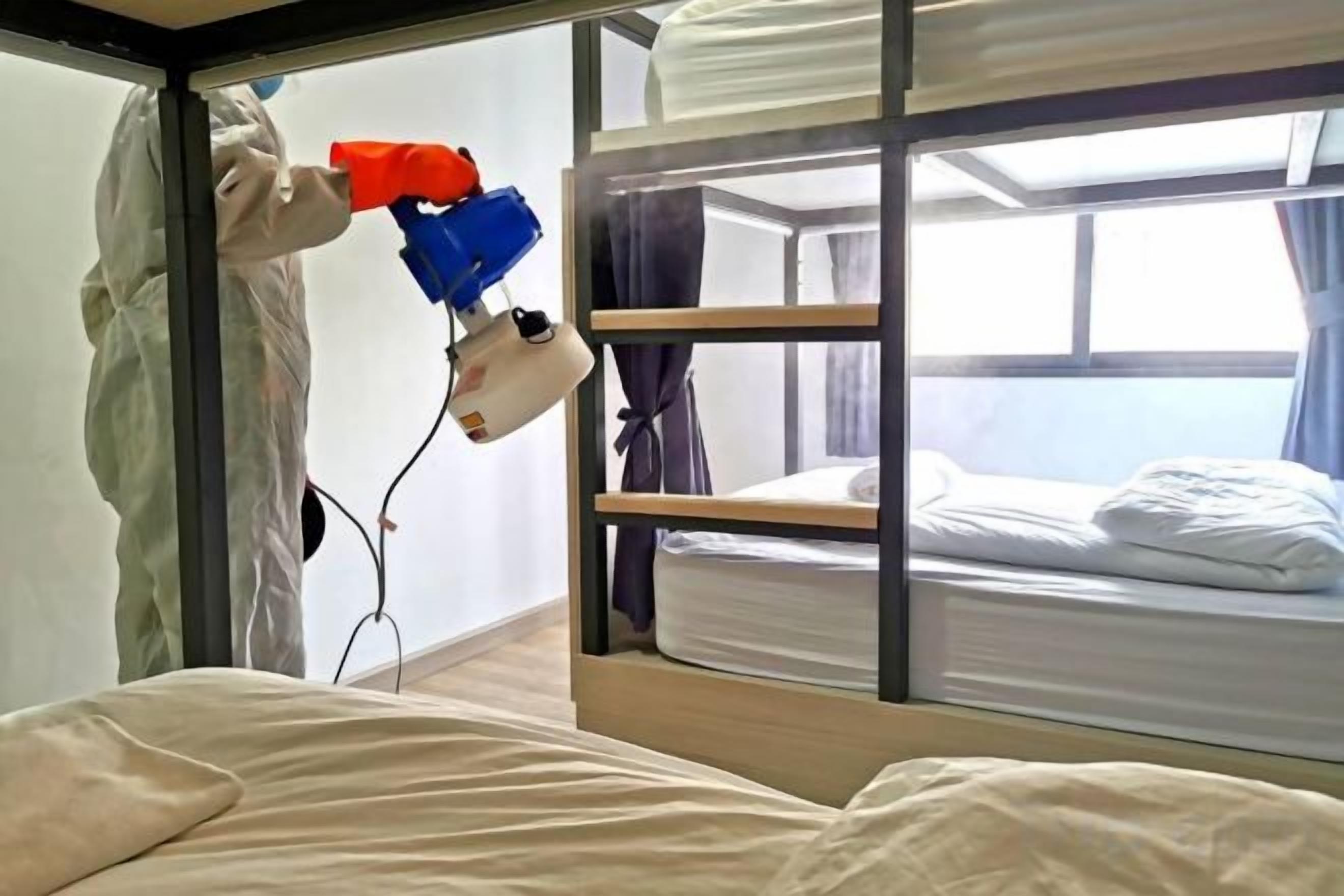 A bunk bed room with a window, a bed with white bedding, and a person using a red and blue device.