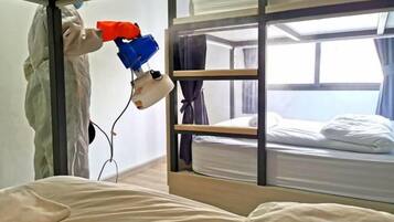 A bunk bed room with a window, a bed with white bedding, and a person using a red and blue device.
