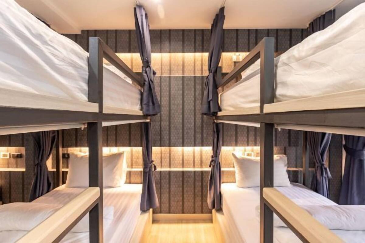 Een slaapkamer met stapelbedden, een centrale gangpad, gordijnen en een behang met een patroon.