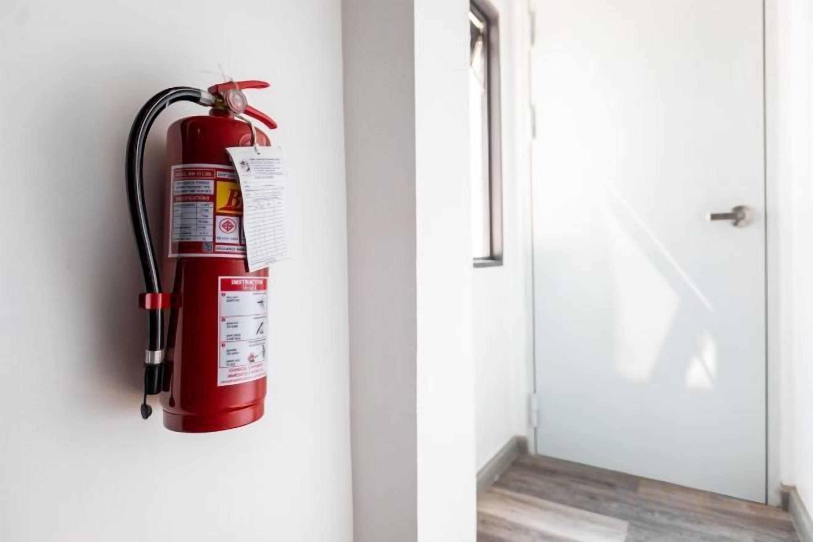A red fire extinguisher mounted on a wall next to a door with a metal handle.
