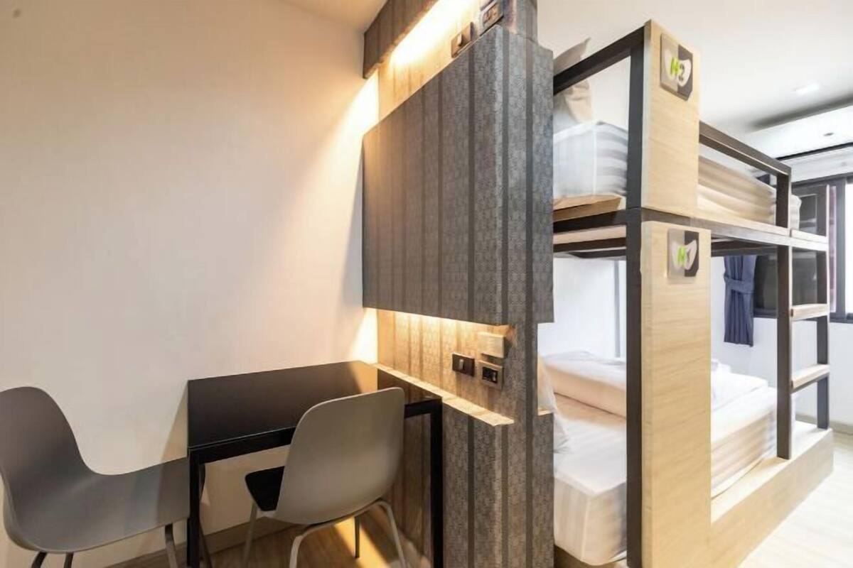 Een stapelbed met een houten hoofdbord, een bureau met stoel en een klein plankje.