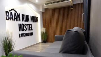 A modern hostel room with a bed, a wall-mounted air conditioner, and a sign indicating the hostel's name.