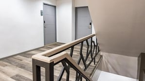 Un pasillo con suelo de madera, barandilla de metal y dos puertas cerradas.