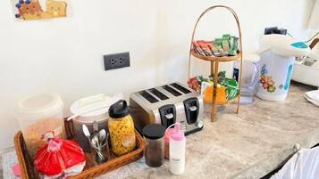 A kitchenette with a toaster, a bread basket, a coffee maker, and various food containers.