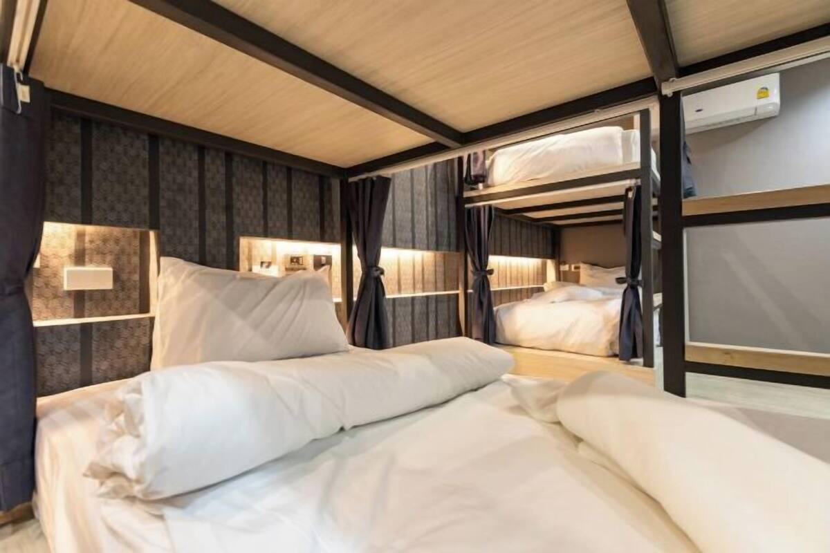 Een slaapkamer met stapelbedden, een houten plafond en lambrisering, een nachtkastje met lamp en een raam met gordijnen.