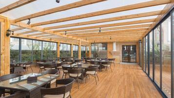 An outdoor dining area with wooden beams, glass walls, and wicker furniture.